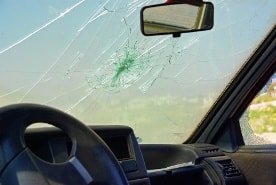 Výměna čelního skla – prasklé sklo kvůli nárazu kamínku. V pozadí lze vidět auto.