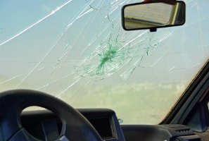 Výměna čelního skla – prasklé sklo kvůli nárazu odlétnutého kamínku. V pozadí lze vidět auto.