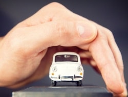 Eine Hand beschützt das mini Modellauto eines alten Fiat