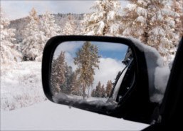 Der linke Außenspiegel eines fahrenden Ford Focus mit dem Winterwald im Spiegelbild