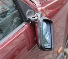 Abgefahrener Außenspiegel eines roten Autos vor der Repatur in einer Werkstatt