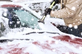 Windschutzscheibe eines roten Autos wird in Winter vom Eis befreit